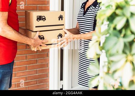 Young hispanic man delivering package to homeowner - Senior woman receiving the parcel box from the delivery worker Stock Photo