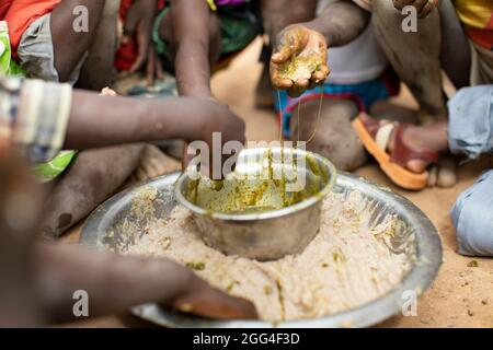 A group of children eat around a communal dish of millet paste and baobab leaf stew, likely their only meal of the day. This extended family has been displaced due to violence and insecurity and now faces hunger and food shortages. Kossi Province, Burkina Faso, West Africa. Stock Photo