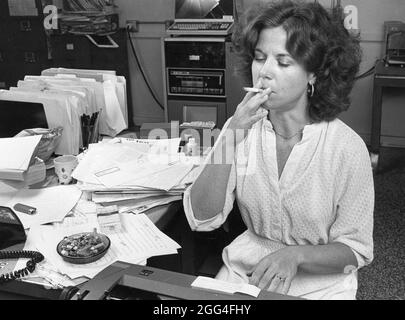 Austin Texas USA, circa 1984: Female reporter smoking  cigarette in newspaper newsroom as deadline approaches. ©Bob Daemmrich Stock Photo