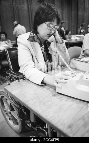 Austin Texas USA, circa 1985: Handicapped woman in wheelchair talks on telephone during fundraising 'phonathon.'  File 85-253 Stock Photo