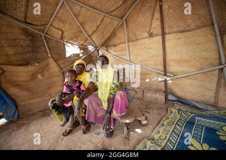 Tolofidje Mariam (26) sits with her daughter Damango Awa (2) and mother, Togo Awa (45), inside the makeshift tent where they sleep. The family fled their home village due to violence and insecurity. Because they cannot farm, they face hunger and food shortages each day.  Sahel 2021 Crisis; Kossi Province, Burkina Faso.  Feb 18, 2021. Photo by Jake Lyell. Stock Photo