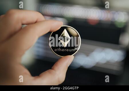 Ethereum cryptocurrency, physical coin close-up held between two fingers Stock Photo