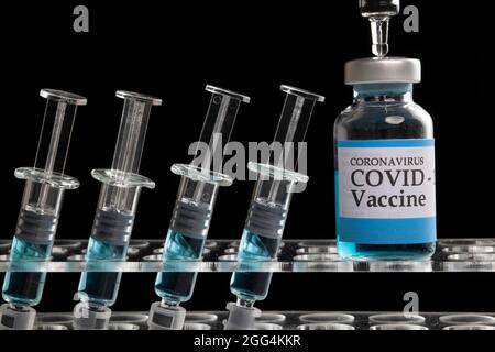 Glass syringes and glass vial filled with blue liquid on a clear plastic rack. Vaccine, vaccination concept. Black background. Stock Photo