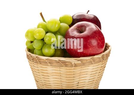 A bunch of green grapes and red apples in a weave bamboo basket. Isolated on white background. Fresh fruit basket. Stock Photo