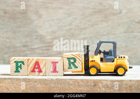 Toy forklift hold letter block r to complete word fair on wood background Stock Photo