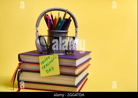 Composition from a stack of colorful books pencils glasses wireless headphones on a yellow background with copy space. Back to school concepts. Teache Stock Photo
