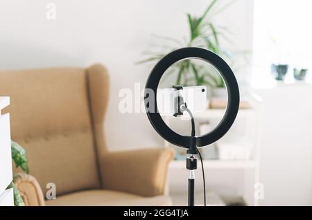 Mobile phone and ring lamp in cozy room at home or office. Equipment for blogging and recording video broadcasts and communicating with social media Stock Photo