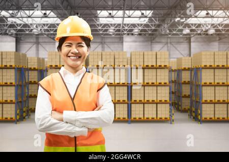 Asian worker in warehouse with stack of cardboard boxes Stock Photo