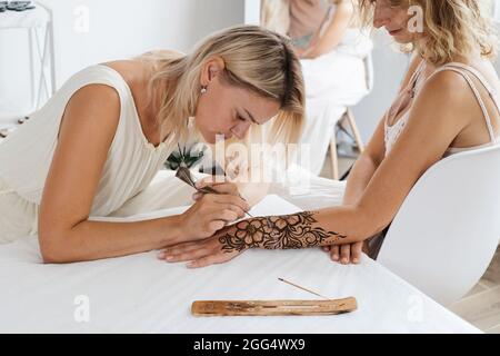 Mehndi artist drawing floral henna tattoo on woman hand in beauty salon. Master applying traditional mehendi pattern for bride before wedding. Stock Photo