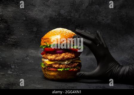 Hand grabbing a big double chicken burger with cheese and vegetables Stock Photo