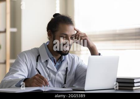 Happy millennial male african american doctor working on computer. Stock Photo