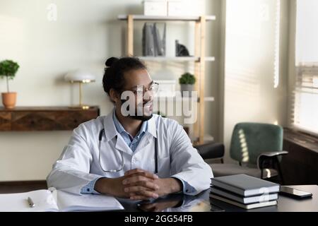 Smiling millennial african american doctor in eyeglasses looking in distance. Stock Photo