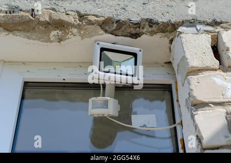 Motion sensor and LED spotlight on the wall of the building. Automatic building perimeter lighting system. Protection of private property. Stock Photo