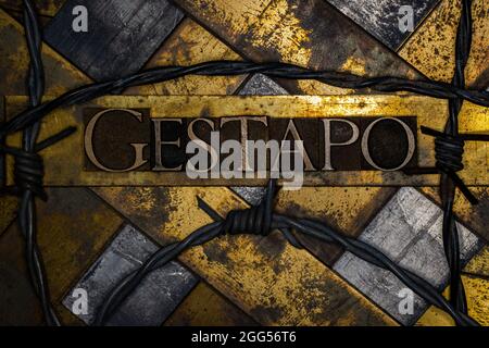 Gestapo text on grunge copper and vintage gold background with barbed wire Stock Photo