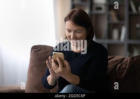 Happy older mature woman using smartphone at home. Stock Photo