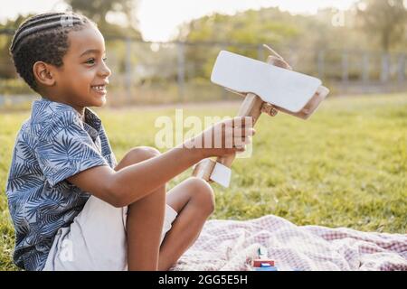 Young african boy playing with wood toy outdoor at city park - Focus on face Stock Photo
