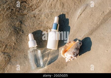 Bottles of cosmetic oil and serum, seashell on natural stone background. Natural moisturising cosmetics concept. Top view, flat lay. Mock up. Stock Photo