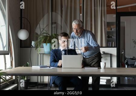 Senior businessman mentor instructing training new employee, using laptop, Stock Photo