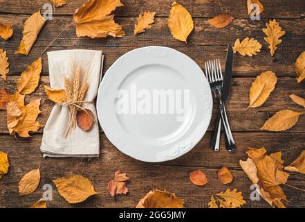 Autumn background with a plate, napkin and cutlery on a wooden background with leaves. Stock Photo