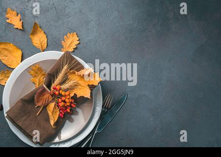 Autumn festive background with plates, serving napkin, berries and autumn leaves on a dark background. Stock Photo
