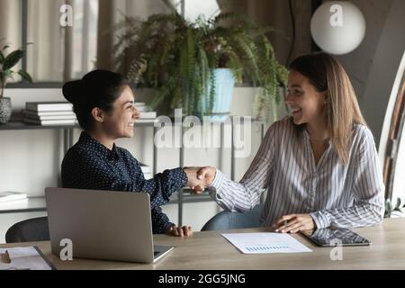 Smiling Indian and Caucasian businesswomen shaking hands at workplace Stock Photo