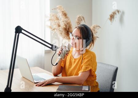 Cheerful woman host streaming his podcast using voice microphone. Female podcaster making audio stream in her small studio Stock Photo