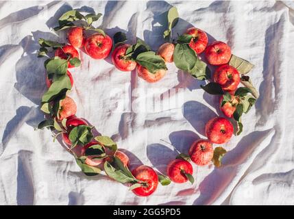 Autumn background of a small red apple and heart-shaped leaves on a beige linen textile background. An empty copy space  Top view Stock Photo