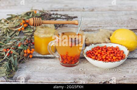 A cup of Hot vitamin Sea buckthorn tea, lemon and ginger are on an old wooden table. Anti-cold kit in the flu season and covid19. herbal medicine Stock Photo