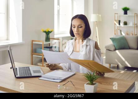 Woman sitting at desk in her home office and reading business letters and documents Stock Photo