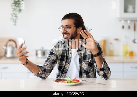 Happy arab man having breakfast and online party via smartphone Stock Photo