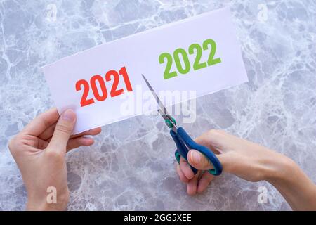 Woman's hand cuts the paper with the words 2021 and 2022 on it with scissors. New year 2022 coming concept. New year new beginning. Stock Photo