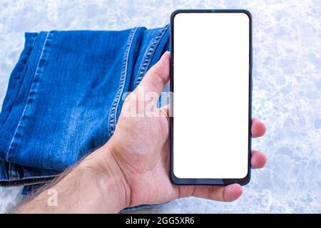 Man hand holding white desktop screen mobile phone. Blue denim jean in the background. Mockup phone image. Stock Photo
