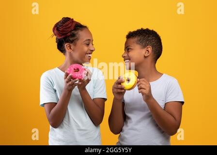 Cheerful black boy and girl eating delicious donuts Stock Photo