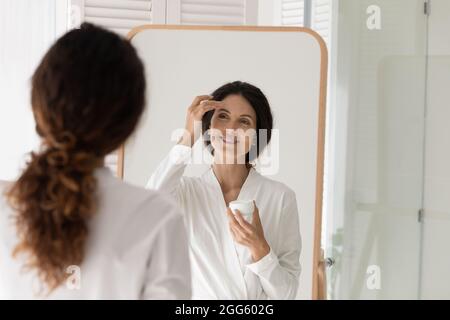 Happy young woman applying moisturizing cream on face. Stock Photo