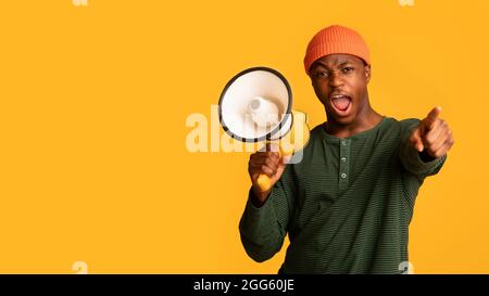 Attention. Emotional Black Guy With Megaphone Shouting And Pointing Finger At Camera Stock Photo