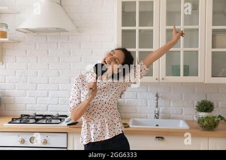 Carefree happy young woman singing song in kitchen. Stock Photo