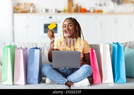 Emotional black woman sitting with credit cards, using laptop Stock Photo