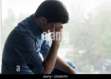 Depressed frustrated millennial man touching head, covering face Stock Photo