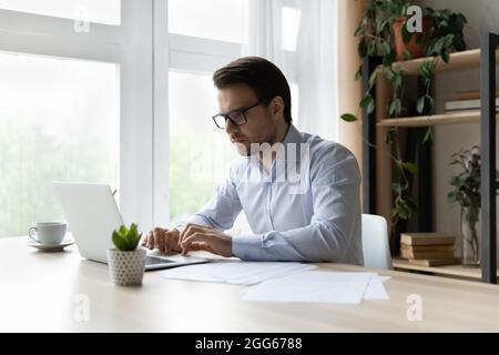 Serious millennial businessman working at laptop in office Stock Photo