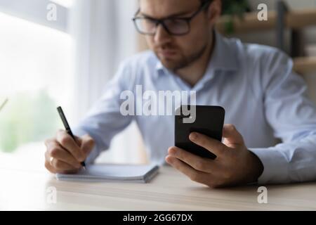 Focused millennial business man using mobile phone and taking notes Stock Photo