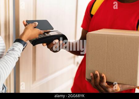 Unrecognizable Black Woman Paying For Delivered Parcel Using Smartphone Indoor Stock Photo