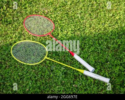 Two simple colorful badminton rackets laying on the grass, closeup, nobody. Leisure, sports recreation equipment symbol, healthy summer outdoor activi Stock Photo