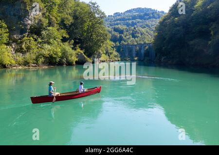 Aerial view of mother and son rowing in a red canoe on Soca river under an old stone bridge near Most na Soci, Avce, Slovenia Stock Photo