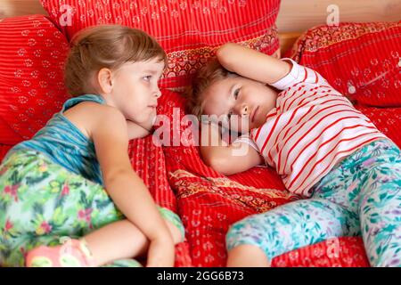 Two little school age girls, healthy young tired exhausted children resting on a bed together. Sisters, siblings laying on the bed at home taking a br Stock Photo