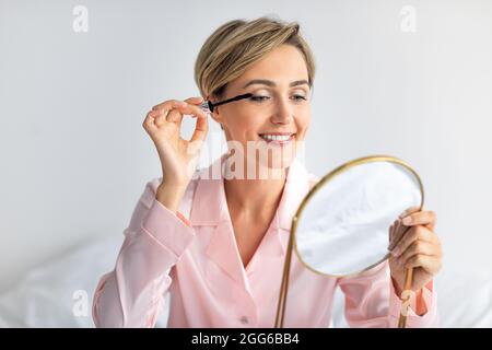 Closeup of smiling woman holding mascara applying makeup Stock Photo