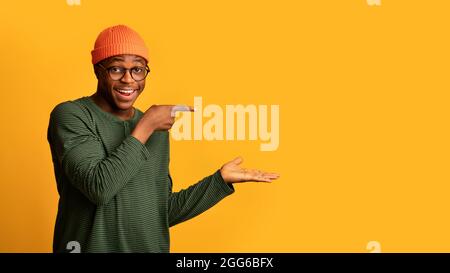 Look At This. Cheerful Black Guy Pointing With Finger At Open Palm Stock Photo
