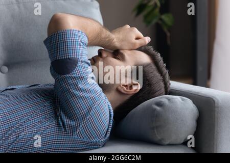 Tired frustrated millennial man lying on sofa at home Stock Photo