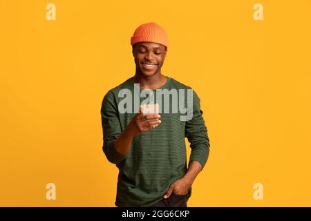 Cool App. Happy young black guy using smartphone, browsing new application Stock Photo