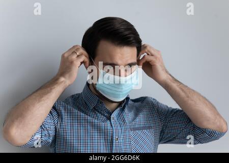 Serious young 30s man putting on face medical mask Stock Photo