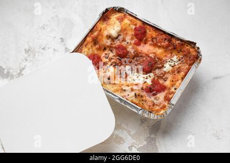 Take Out Creamy Lasagna with fresh mozzarella and tomatoes on white clay background Stock Photo